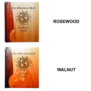 K&ouml;nnte beinhalten: H&ouml;lzerne Abenteuerb&uuml;cher mit graviertem Weltkarten-Design. Das obere Buch ist aus Rosenholz und das untere Buch aus Walnussholz. Jedes Buch tr&auml;gt den Text "Our Adventure Book" und einen Familiennamen.