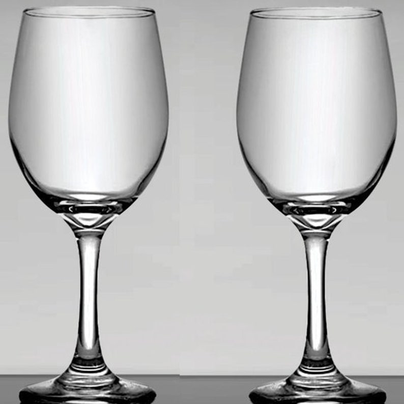 May include: Two clear wine glasses with a classic design. The glasses have a rounded bowl, a slender stem, and a flat base. The glasses are made of transparent glass and are set against a light gray background.