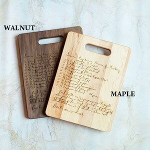 Pode incluir: Duas t&aacute;buas de corte de madeira, uma de nogueira e outra de bordo, cada uma com formato retangular e uma al&ccedil;a. As t&aacute;buas apresentam receitas manuscritas. A t&aacute;bua de nogueira &eacute; marrom escuro, enquanto a de bordo &eacute; clara.