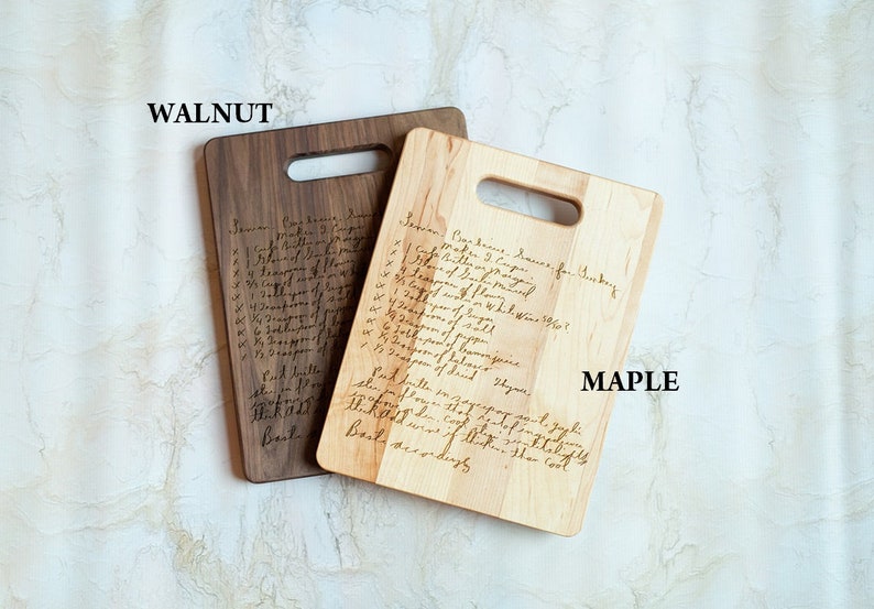 Pode incluir: Duas t&aacute;buas de corte de madeira, uma de nogueira e outra de bordo, cada uma com formato retangular e uma al&ccedil;a. As t&aacute;buas apresentam receitas manuscritas. A t&aacute;bua de nogueira &eacute; marrom escuro, enquanto a de bordo &eacute; clara.