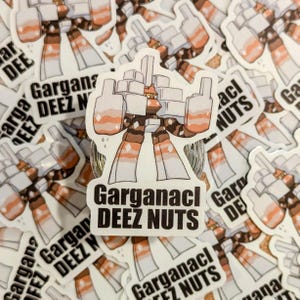 May include: A white sticker featuring a cartoon character with a brown and white color scheme. The sticker has the text "Garganacl DEEZ NUTS" in black. Other stickers with the same design are in the background.
