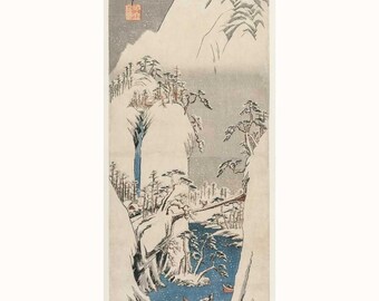 Op de afbeelding: Een Japanse houtsnede die een besneeuwde berg scène afbeeldt met een rivier die door een vallei stroomt. Twee kleine boten zijn zichtbaar in de rivier, en de bergen zijn bedekt met sneeuw. De print is in tinten blauw, wit en grijs.