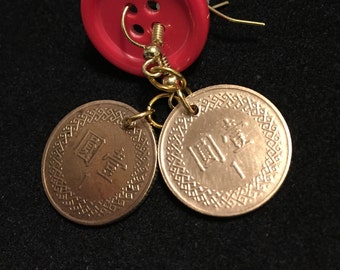 May include: A pair of earrings featuring two gold Chinese coins with the Chinese character for "yuan" and the number "1" on each coin. The coins are attached to a red button with gold accents.