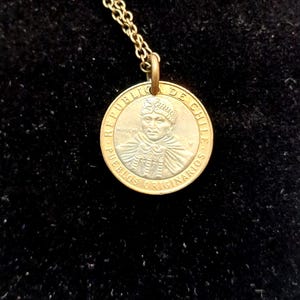 May include: A gold chain necklace with a silver coin pendant featuring a portrait of a person with the text "REPUBLICA DE CHILE" and "PUEBLOS ORIGINARIOS" around the edge.