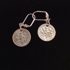 May include: A pair of silver earrings with a United States dime attached to each earring. The dimes are silver and have the words "United States of America" and "One Dime" on them.
