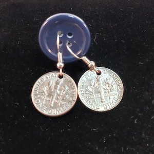 May include: A pair of silver earrings with a United States dime coin as the dangle. The dimes are dated 1964 and feature the image of Lady Liberty.