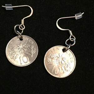 May include: A pair of silver earrings featuring a 10 cents coin from Singapore with a floral design. The coin is attached to a silver hook earring.