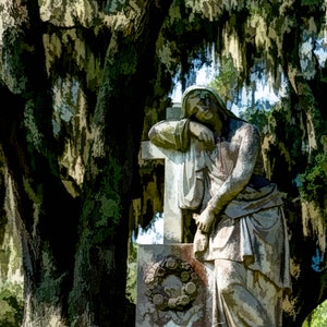 May include: A white marble statue of a woman leaning against a cross. The statue is in a cemetery, with a large oak tree in the background. The statue is weathered and has a vintage look.
