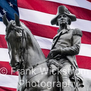 Può includere: Una statua di bronzo di un uomo a cavallo, con un cappello e un'uniforme militare, si erge davanti a una bandiera americana. La statua è un monumento a una figura storica.