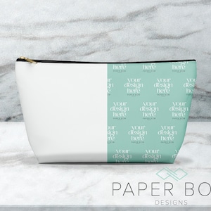 May include: White zippered pouch with a black zipper and a teal and white pattern on the right side. The pattern repeats the text "Your design here" and "Paper Bow". The pouch is sitting on a white marble surface. The text "Paper Bow Designs" is printed in black below the pouch.