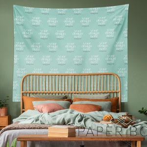 May include: A light blue tapestry with the text "Your design here" repeated in a grid pattern hangs on a green wall behind a wooden bed frame with a light green, brown, and beige bedding set. The bed is styled with a throw blanket, pillows, and a book on a wooden table.