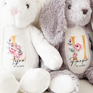 May include: Two plush bunny toys, one white and one gray, with personalized embroidery. The white bunny has the name "Lyra" and the date "07.10.2022" embroidered on it. The gray bunny has the name "Harper" and the date "07.10.2022" embroidered on it.
