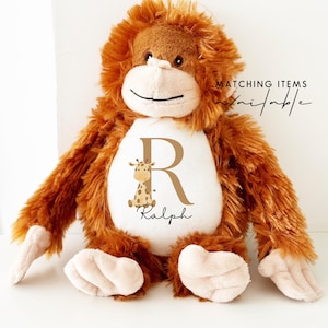 Peut inclure: Un singe en peluche marron avec un t-shirt blanc sur lequel est dessiné un girafe marron et la lettre R, avec le nom Ralph écrit en dessous.