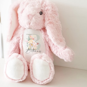 May include: Pink plush bunny with a white patch on its chest. The patch features a floral design with the letter "B" and the name "Bethany" written in cursive.