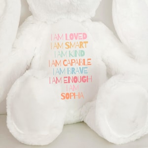 May include: White plush bunny with the text "I AM LOVED", "IAM SMART", "I AM KIND", "I AM CAPABLE", "I AM BRAVE", "TAM ENOUGH", "IAM", "SOPHIA" printed on the front.
