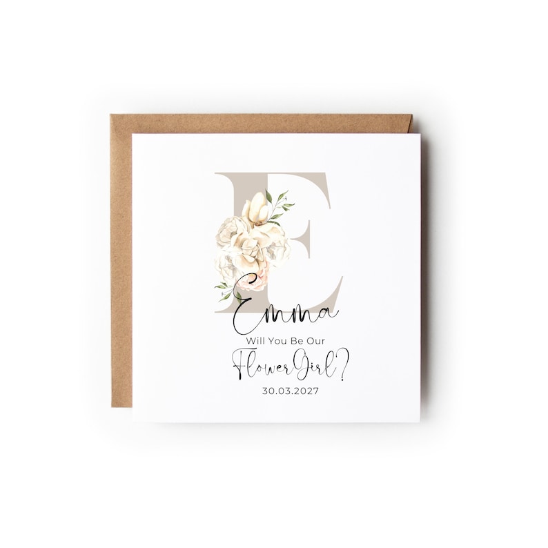 May include: A white card with a floral design and the letter E. The text on the card reads "Emma Will You Be Our Flower Girl? 30.03.2027"