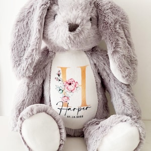 May include: A gray plush bunny with a white patch on its chest. The patch features a gold letter H with pink floral accents and the name "Harper" with the date "07.10.2022" underneath.