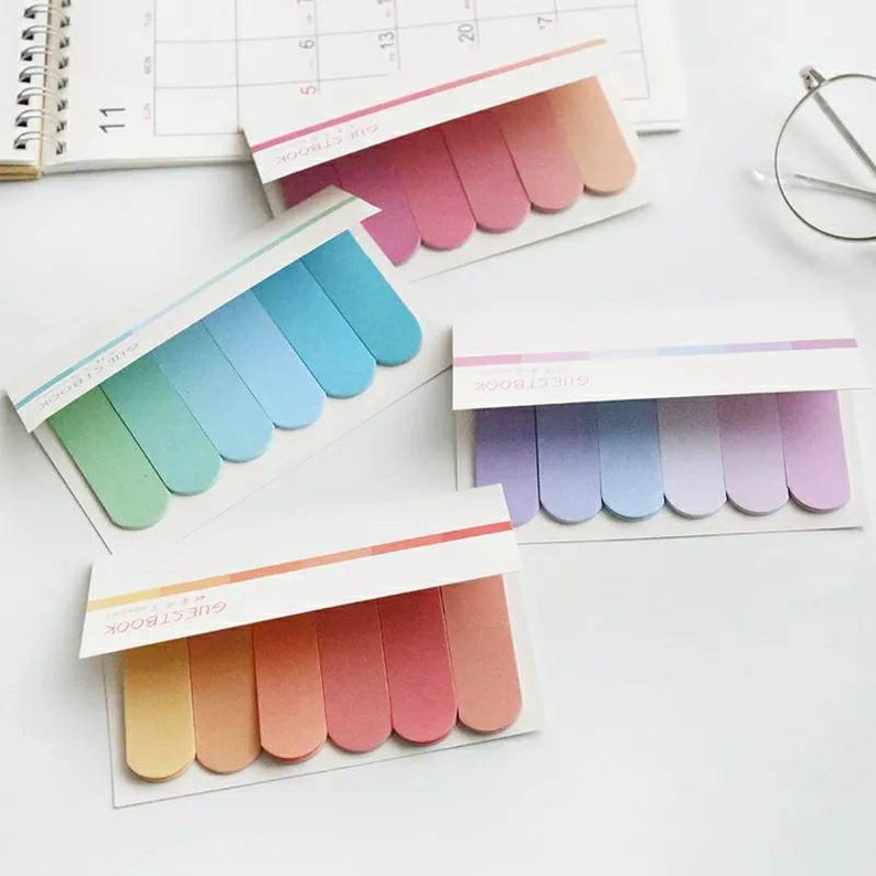 May include: Four sets of colorful sticky notes with rounded edges. Each set has five notes in a gradient of colors, including pink, blue, green, and orange. The notes are labeled "GUESTBOOK" and "STICKERBOOK".
