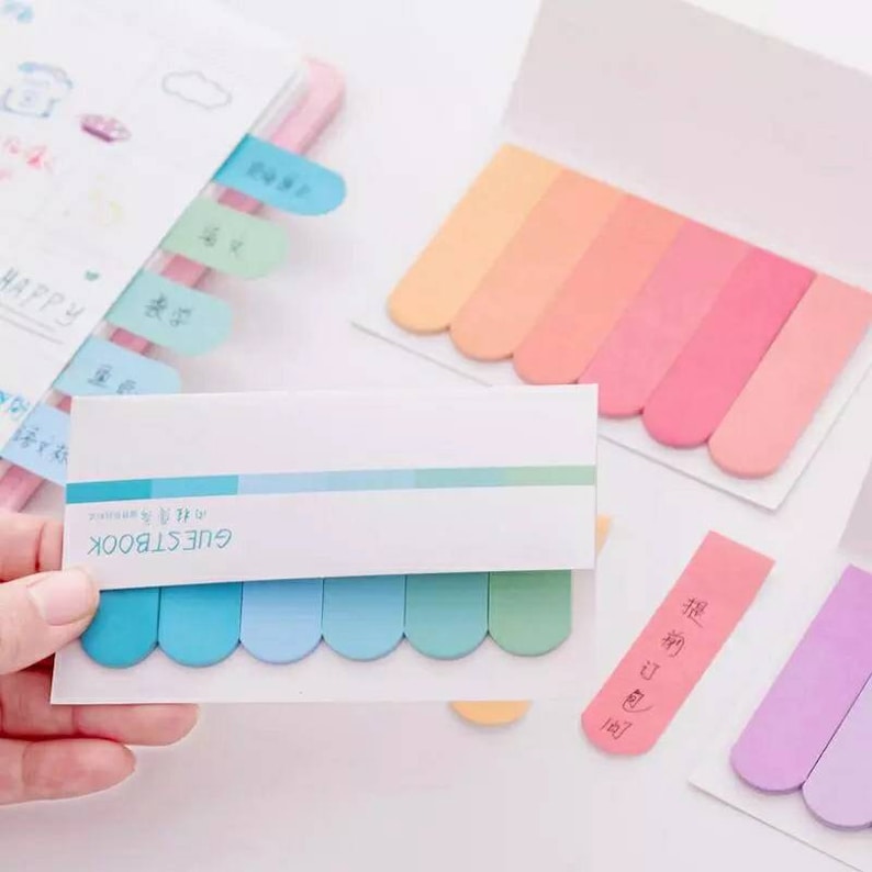 May include: A set of colorful sticky notes with rounded edges. The notes are in various shades of blue, pink, and purple. The notes are labeled "GUESTBOOK" and have the text "Happy Birthday" written on them.