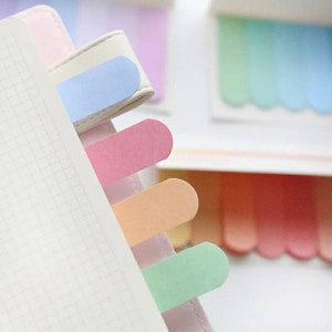 May include: A set of colorful sticky notes with rounded edges. The notes are in shades of blue, pink, peach, and green. The notes are attached to a notebook with a white tab.
