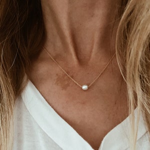 Puede incluir: Un delicado collar de cadena dorada con un solo colgante de perla blanca.