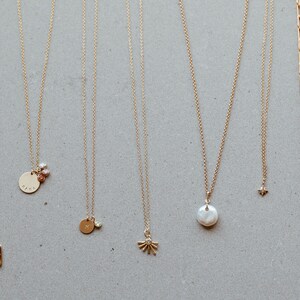 Puede incluir: Una colecci&oacute;n de diez collares de oro con diferentes colgantes, incluyendo una flor, una estrella, una perla, un c&iacute;rculo y un cuadrado. Los collares se muestran sobre un fondo gris claro.