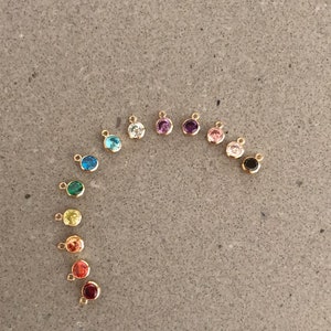 May include: A rainbow assortment of small, round, gold-toned charms with colorful gemstones. Each charm has a small loop for attaching to a necklace or bracelet.