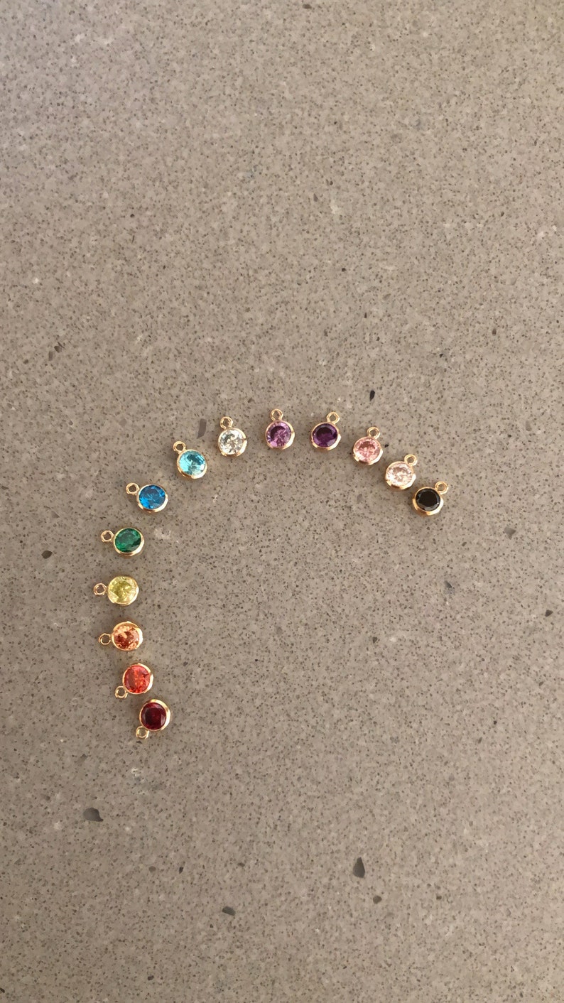 May include: A rainbow assortment of small, round, gold-toned charms with colorful gemstones. Each charm has a small loop for attaching to a necklace or bracelet.