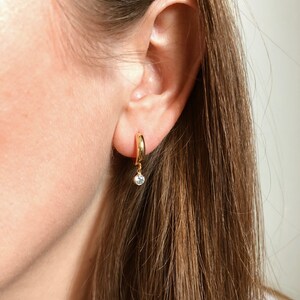 May include: Gold hoop earrings with a small dangling clear stone.