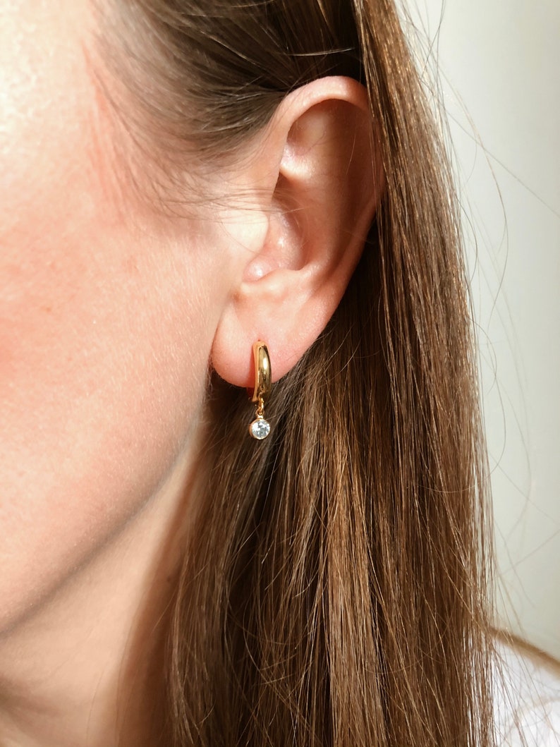 May include: Gold hoop earrings with a small dangling clear stone.