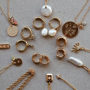 May include: A collection of gold necklaces and earrings with various charms, including a pearl, a flower, a star, and a bar with three small diamonds. Some of the charms have small gemstones.