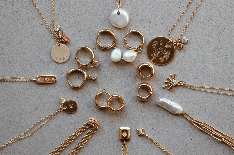 May include: A collection of gold necklaces and earrings with various charms, including a pearl, a flower, a star, and a bar with three small diamonds. Some of the charms have small gemstones.
