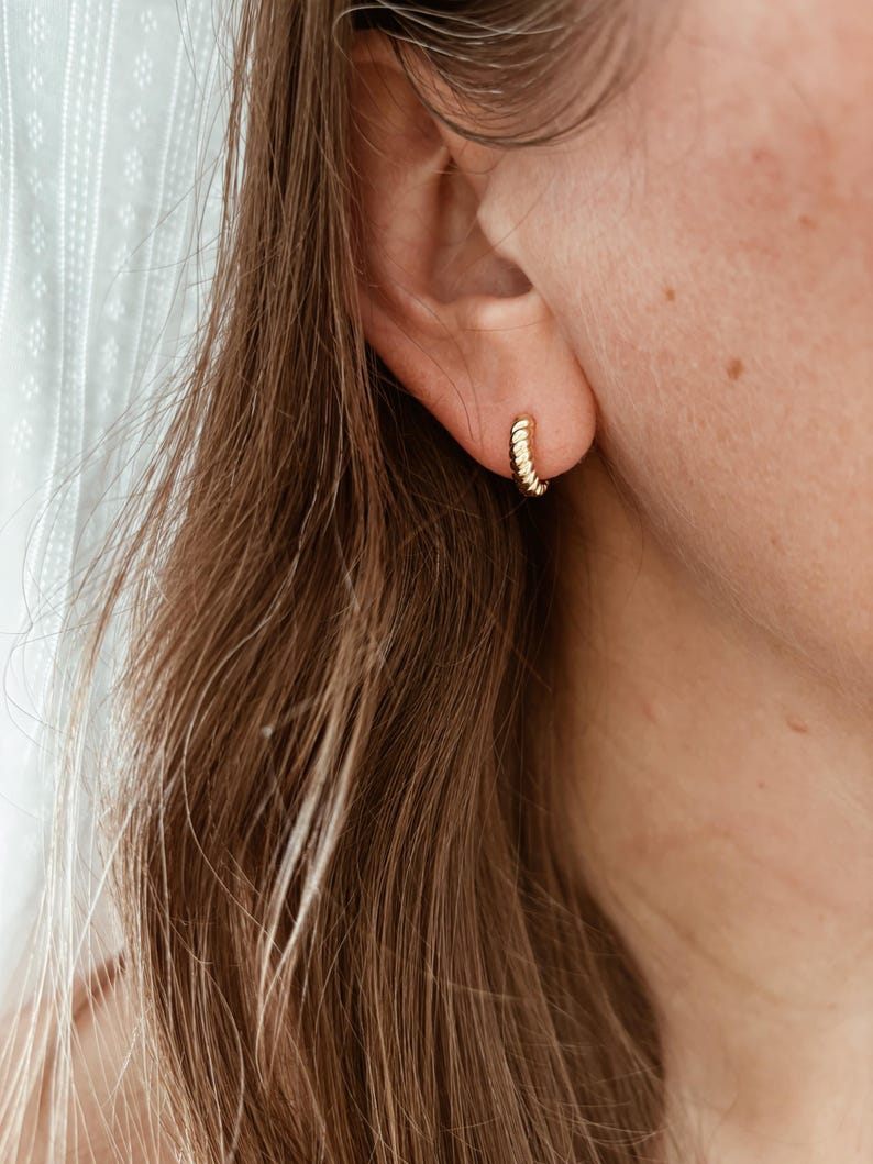 K&ouml;nnte beinhalten: Nahaufnahme eines Ohrs, das einen goldenen Creolen-Ohrring tr&auml;gt. Der Ohrring besteht aus einem gedrehten Drahtdesign.