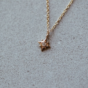 Puede incluir: Un collar de cadena dorada con un peque&ntilde;o colgante de estrella con una sola piedra transparente en el centro.