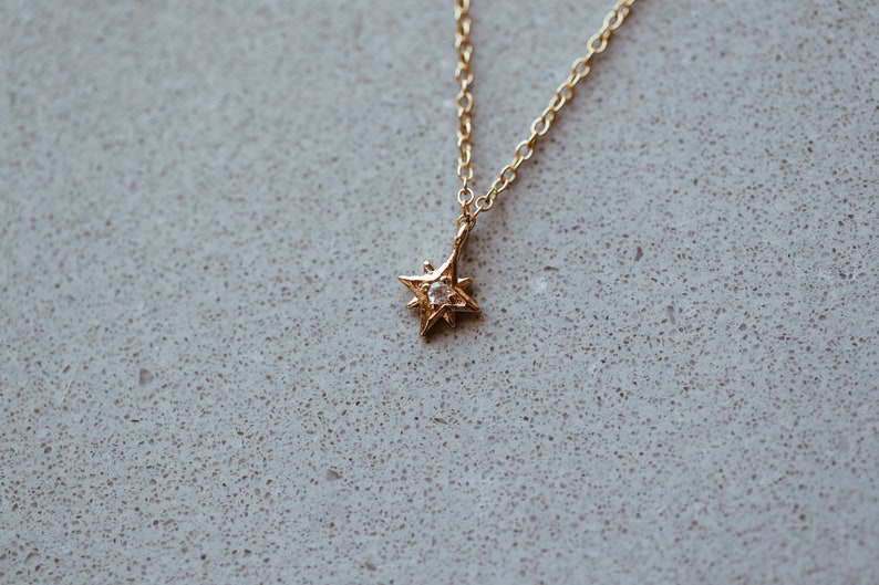 Puede incluir: Un collar de cadena dorada con un peque&ntilde;o colgante de estrella con una sola piedra transparente en el centro.