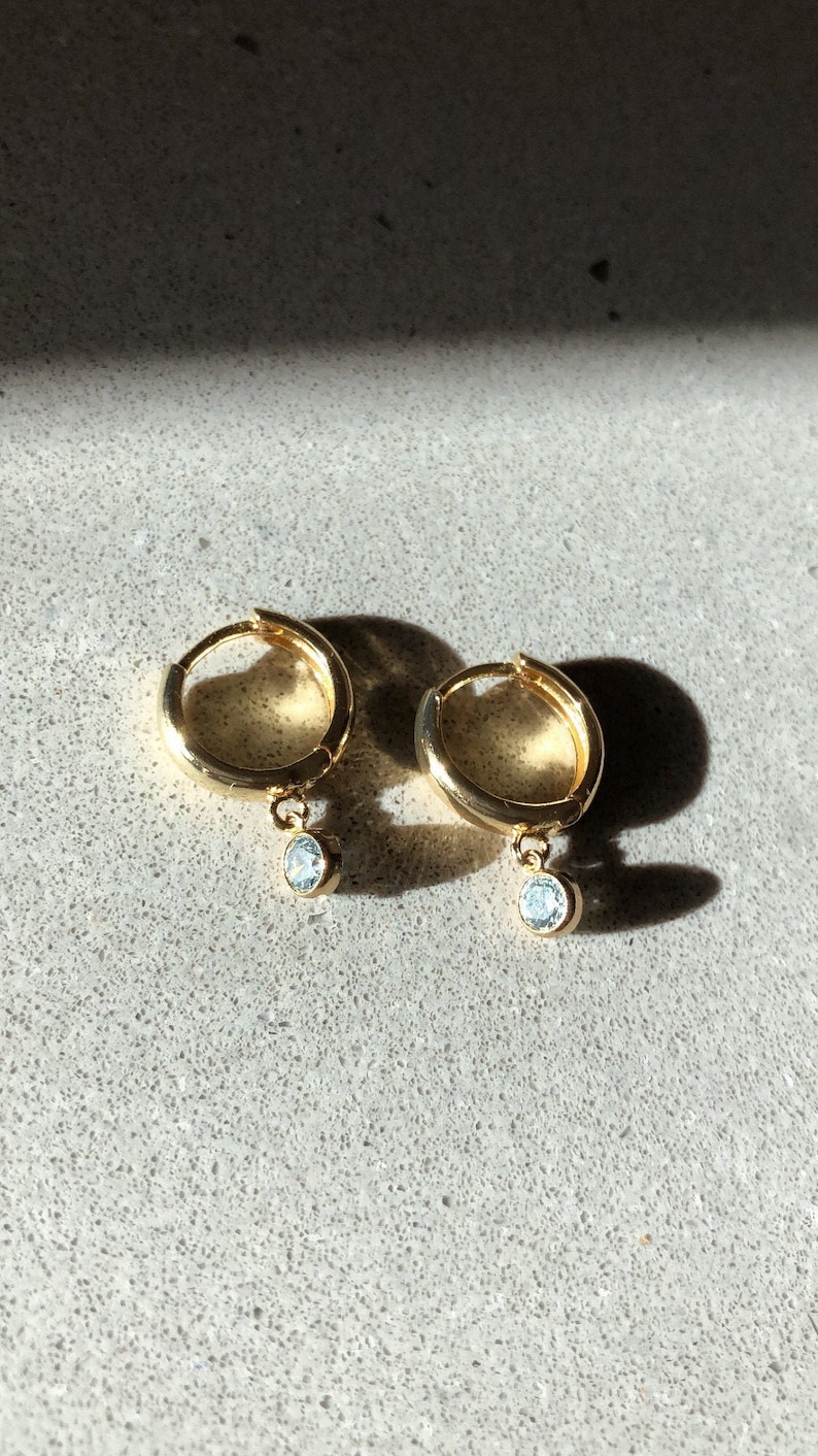 May include: A pair of gold hoop earrings with a small, clear stone dangling from each hoop.