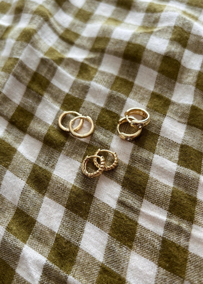 K&ouml;nnte beinhalten: Ein Set mit vier goldenen Creolen. Zwei Paar Ohrringe sind schlichte goldene Creolen, die anderen beiden Paar haben einen kleinen, klaren Stein als Akzent.
