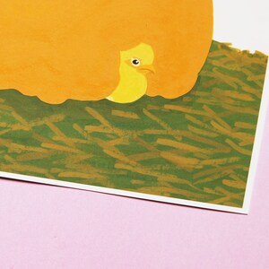 May include: A yellow bird with a closed eye is peeking out from under a large orange object. The bird is sitting on a bed of green and brown grass.
