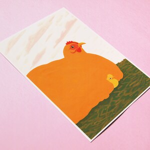 May include: A bright orange hen with a red comb and wattle sits on a bed of green grass with a small yellow chick nestled under her wing.
