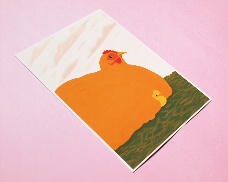 May include: A bright orange hen with a red comb and wattle sits on a bed of green grass with a small yellow chick nestled under her wing.