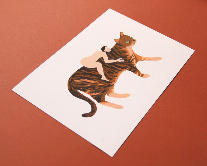 May include: A brown and black striped cat with green eyes is lying down. A nude person is sitting on the cat's back and hugging the cat's neck.