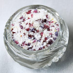 May include: A clear glass jar filled with white, pink, and purple crystals. The crystals are small and sparkly, and they are arranged in a random pattern.
