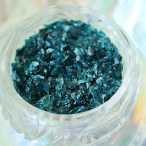 Könnte beinhalten: Eine klare Glasschüssel gefüllt mit tealblauen Glasstücken. Die Glasstücke sind klein und unregelmäßig geformt.