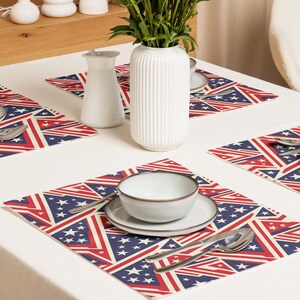 Può includere: Una tavola apparecchiata con quattro tovagliette dal design patriottico. Ogni tovaglietta presenta strisce rosse e bianche, campi blu con stelle bianche e uno sfondo color crema. Un vaso e una brocca bianchi sono anche sul tavolo.