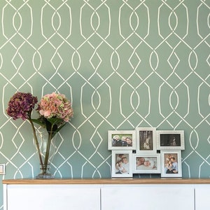 May include: White dresser with six drawers against a green wall with a geometric pattern. The dresser has a wood top and is in a room with a wooden door and a chair.