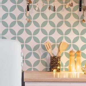 Puede incluir: Interior de cocina con un mueble blanco y una encimera de madera. La pared tiene un patrón repetitivo de círculos superpuestos de color azul claro. Utensilios de madera en un soporte tejido y una cesta tejida sobre la encimera.