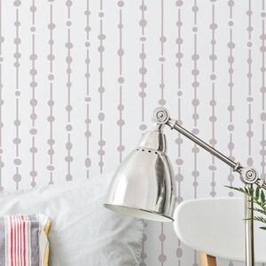 May include: A bedroom with a bed with a striped comforter and pillows. A bedside table with a lamp, a mug, and a vase of white flowers. The wall behind the bed has a light gray and white geometric pattern.