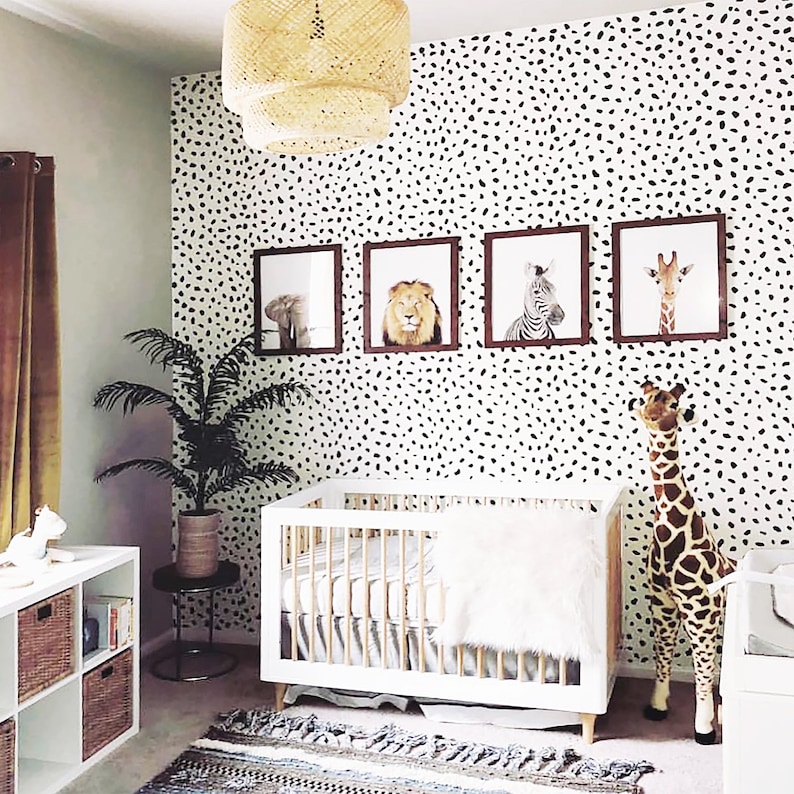 May include: A white crib with a white and gray patterned mattress and a white furry blanket. A stuffed giraffe stands next to the crib. The wall behind the crib is covered in black and white polka dots. There are four framed pictures of animals on the wall.
