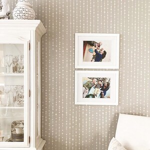 May include: A beige wall with a white bead pattern wallpaper. Two white picture frames with family photos are hung on the wall.
