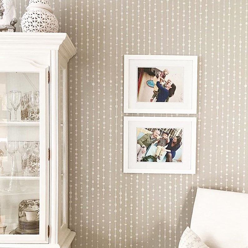 May include: A beige wall with a white bead pattern wallpaper. Two white picture frames with family photos are hung on the wall.